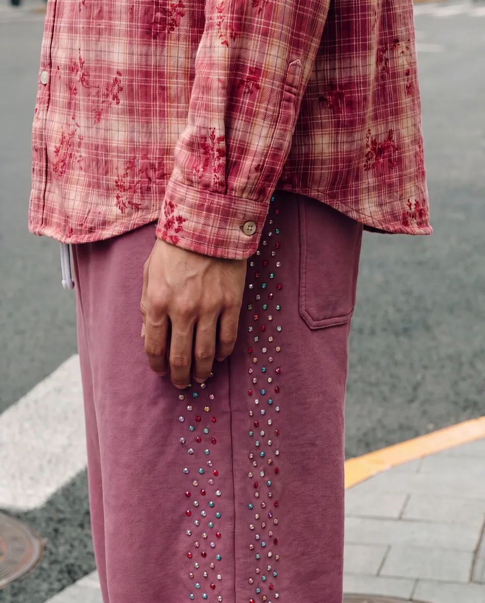 Close crop of the shirt hem and a trouser seam lined with small multicoloured crystals.