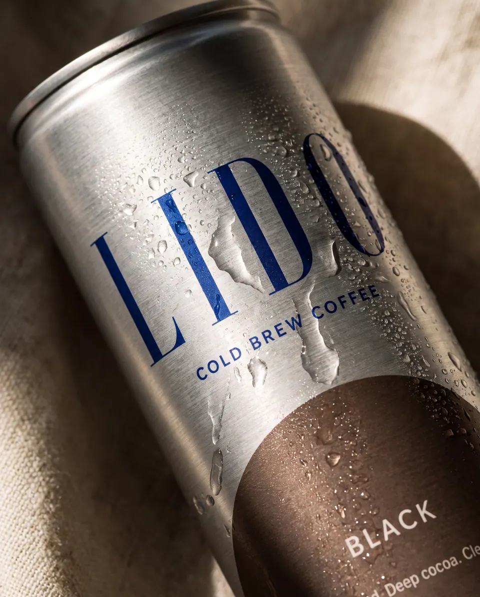 Close-up of a LIDO Black can with condensation on brushed aluminium, resting on linen.