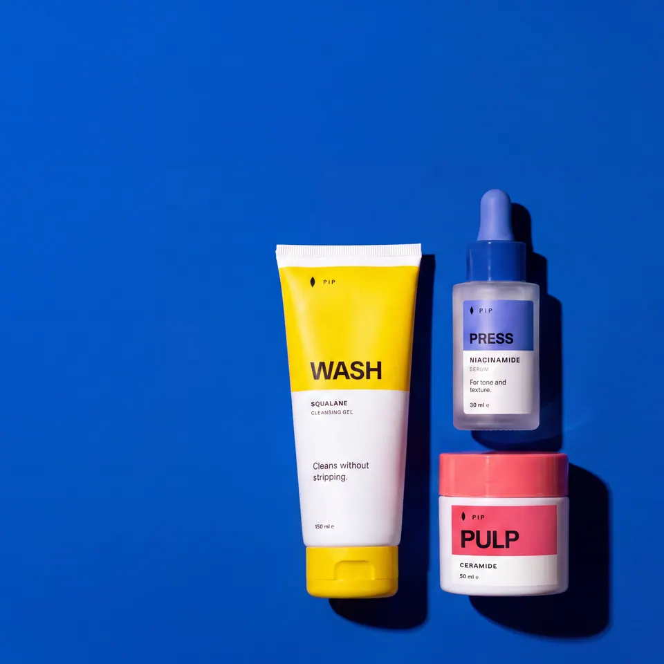 Pip WASH tube, PRESS dropper bottle and PULP jar together on a saturated cobalt-blue background with hard shadows.